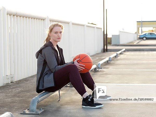 Young female basketball player sitting in parking lot