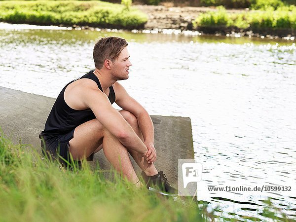 Junger Mann im Sport am Flussufer sitzend