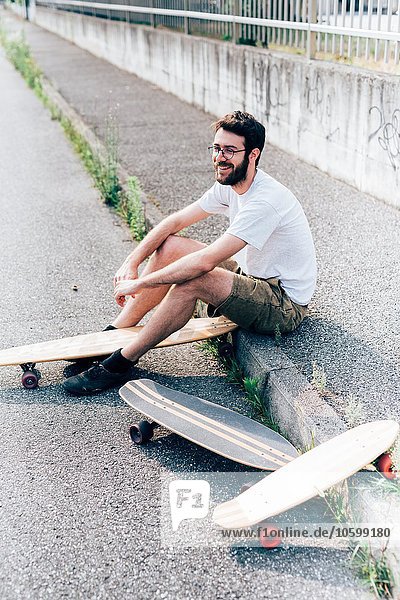 Junger Mann auf Bordsteinkante mit drei Skateboards
