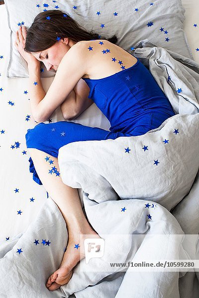 Overhead-Ansicht einer reifen Frau im blauen Pyjama  die in einem sternenbedeckten Bett liegt.