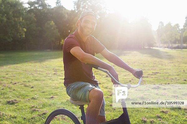 Portrait eines jungen Mannes auf dem Fahrrad im sonnigen Park