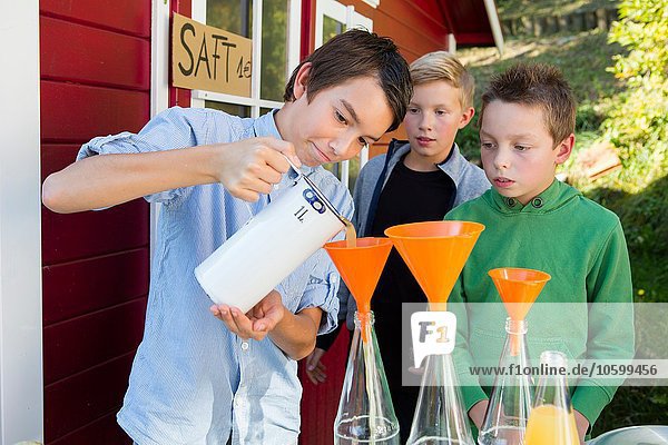 Teenager Jungen und Brüder gießen frischen Orangensaft zum Verkauf am Straßenrand.