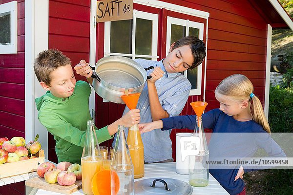 Teenage boy and siblings pouring fresh orange juice to sell at roadside
