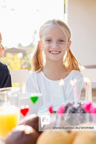 Porträt eines glücklichen Mädchens mit Geburtstagskuchen am Terrassentisch