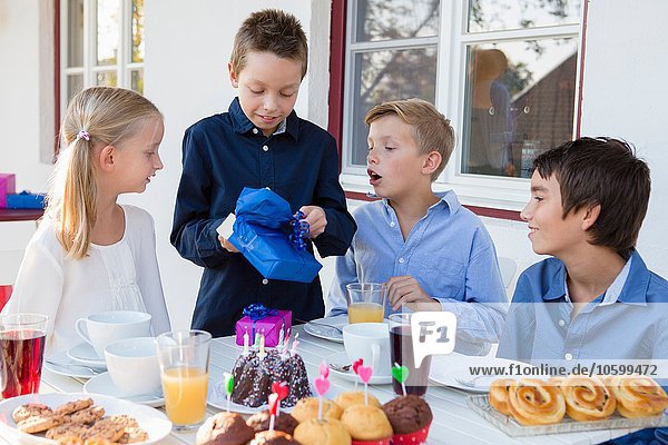 Boy with siblings unwrapping birthday gifts on patio