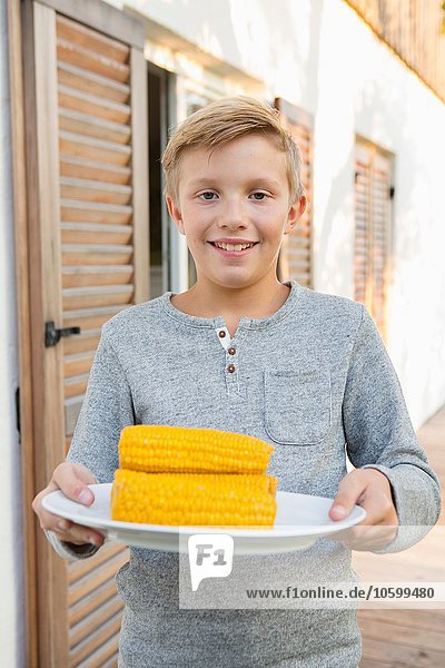 Portrait des Jungen mit Maiskolbenteller zum Grillen im Garten