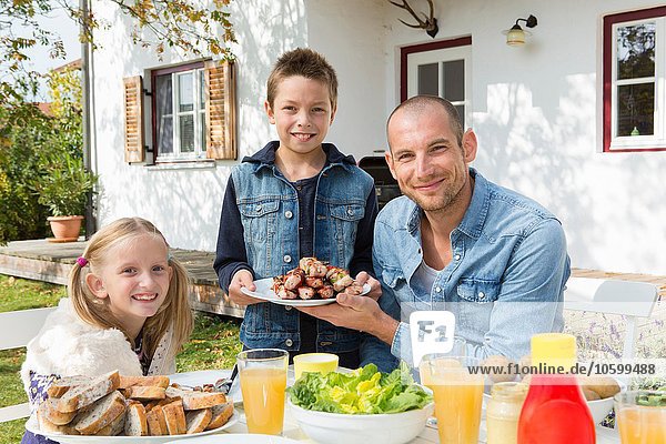 Portrait of father and children at garden barbecue table