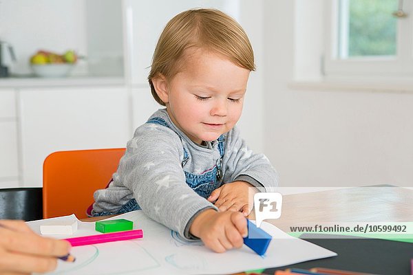 Female toddler using eraser whilst drawing at kitchen table