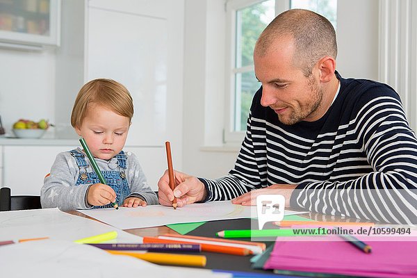 Mid adult man and toddler daughter drawing at kitchen table