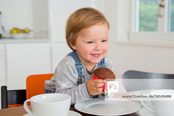Süßes weibliches Kleinkind mit Muffin am Küchentisch