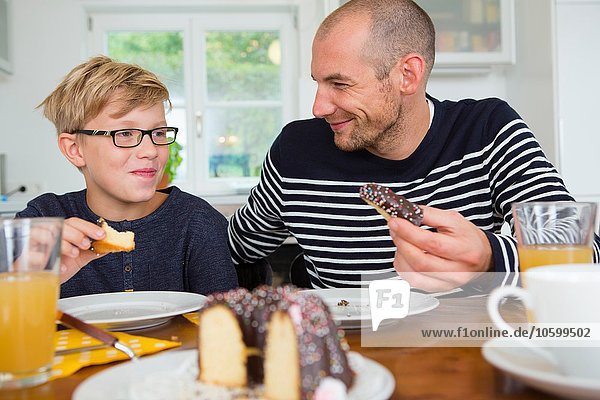 Mid adult man and son eating cake at kitchen table