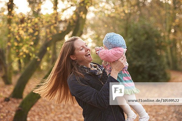 Mid adult woman swinging baby daughter in autumn park