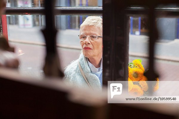Reife Frau mit gelbem Blumenstrauß Schaufensterbummel