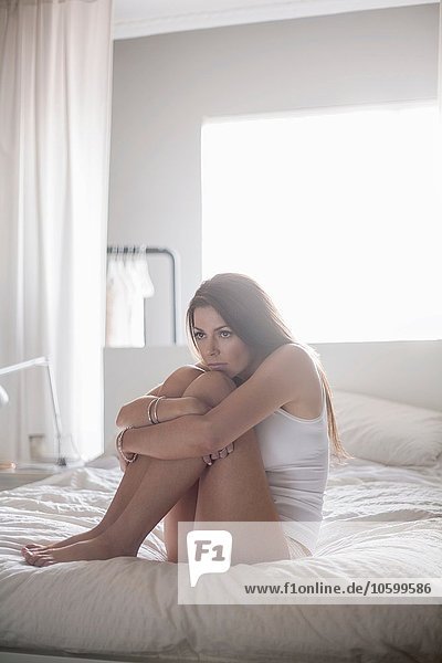 Junge Frau auf dem Bett sitzend Knie umarmend