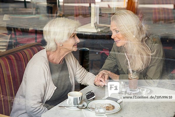 Mother and daughter sitting together in cafe  holding hands  seen through cafe window