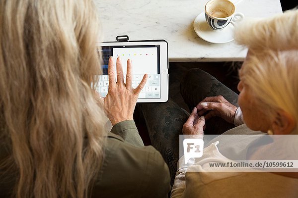 Mutter und Tochter sitzen zusammen im Cafe  Blick auf digitales Tablett  Rückansicht