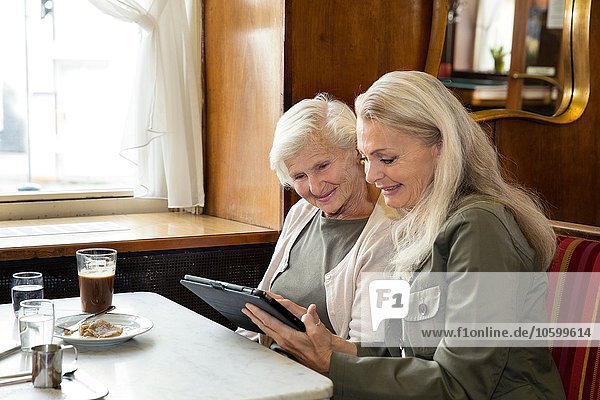Mutter und Tochter sitzen zusammen im Café und schauen auf das digitale Tablett.