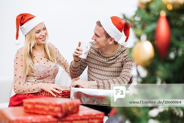 Junger Mann trinkt Kaffee mit Freundin umgeben von Weihnachtsgeschenken