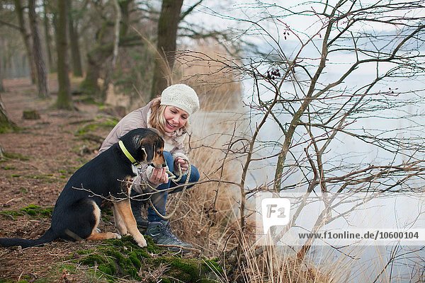 Mittlere erwachsene Frau kauernd mit ihrem Hund am Flussufer