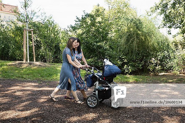 Young woman and mother and pushing baby carriage in park