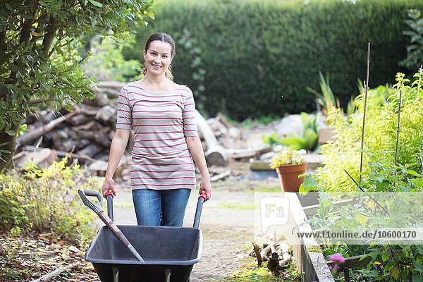 Portrait of female gardener pushing wheelbarrow in rustic organic garden