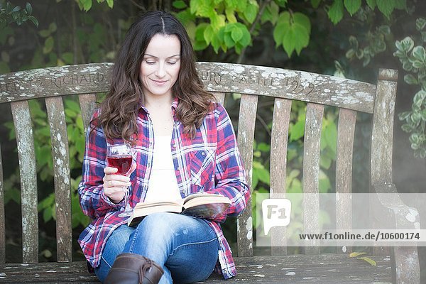 Mittlere erwachsene Frau beim Lesen und Trinken von Rotwein auf der Gartenbank im Thornbury Castle  South Gloucestershire  UK