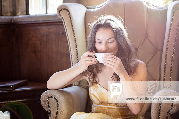 Woman drinking cup of tea in old armchair at Thornbury Castle  South Gloucestershire  UK