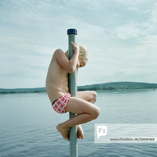 Girl climbing on pole by lake
