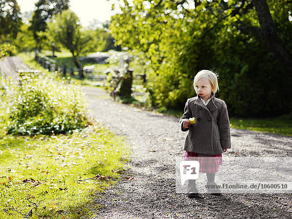 Mädchen isst Obst und steht auf einem Gartenweg