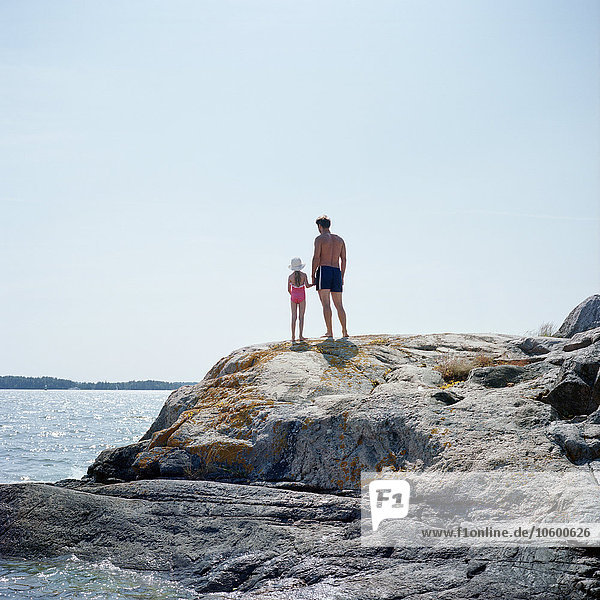 Father and daughter standing on rock by sea  rear view
