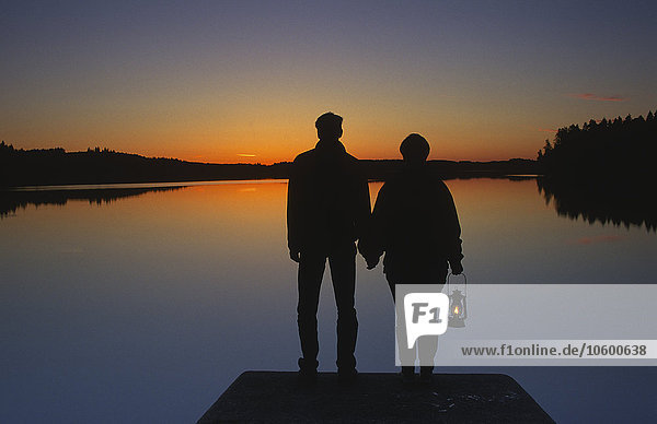 Ein Paar steht bei Sonnenuntergang auf einem Steg  Schweden.