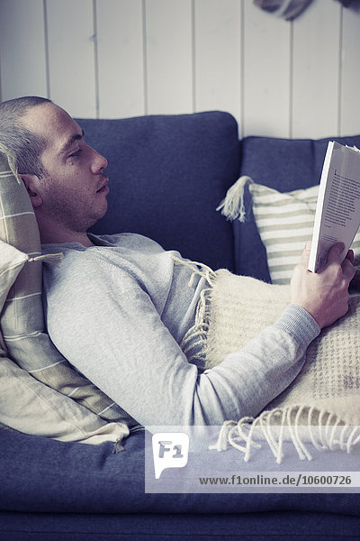 Mann auf Couch liegend  Buch lesend