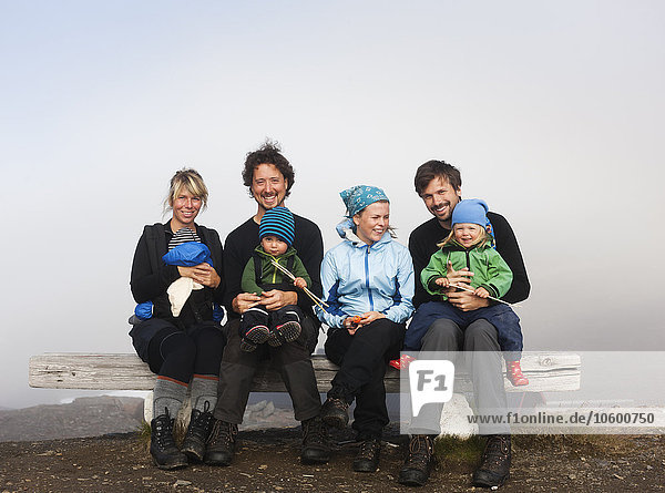 Zwei Paare mit ihren Kindern sitzen auf einer Bank