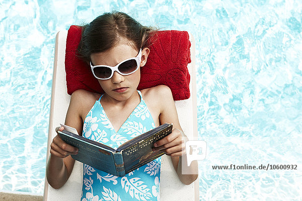 Mädchen liest auf einem Floß am Pool