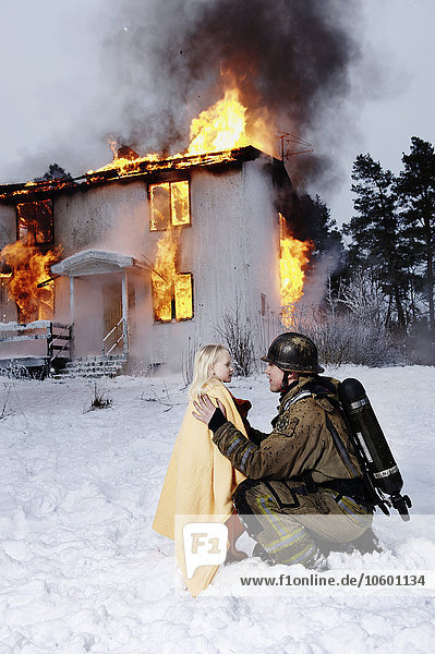 Feuerwehrmann hält gerettetes Mädchen  brennendes Gebäude im Hintergrund