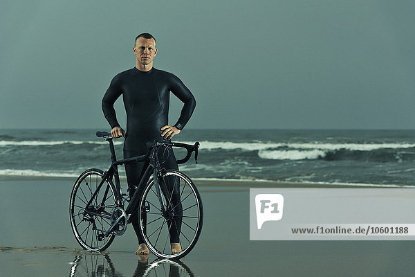 Man wearing wetsuit with bicycle on beach