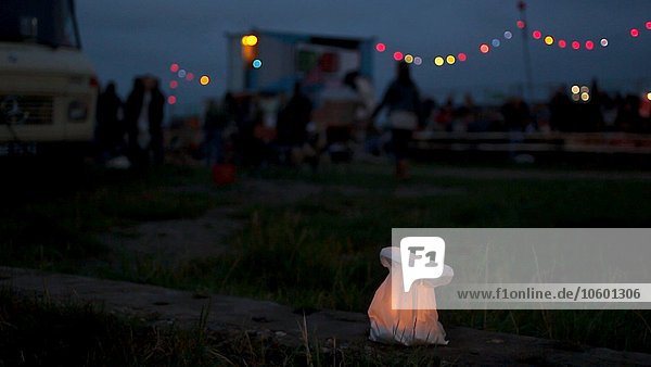 Flackernde Kerze in der Nacht mit verschwommener Menschenmenge auf dem Festival im Hintergrund