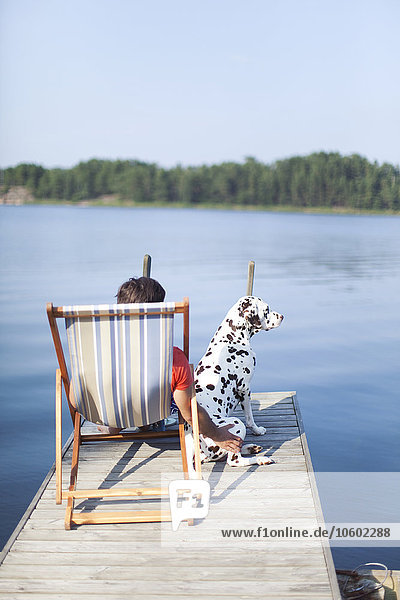 Mann sitzt mit Dalmatiner auf dem Steg  Finnland