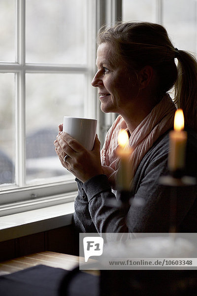Frau trinkt Kaffee und schaut durch ein Fenster