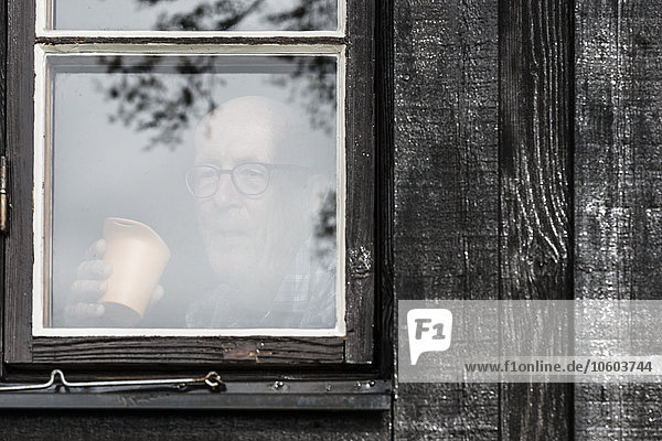 Älterer Mann schaut durch ein Fenster