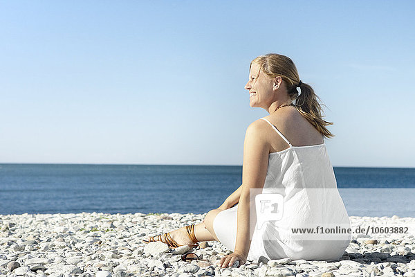 Smiling woman sitting on pebble beach