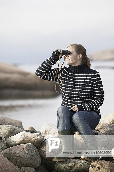Frau betrachtet das Meer durch ein Fernglas