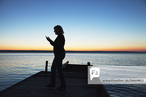 Frau schaut bei Sonnenuntergang auf ihr Mobiltelefon
