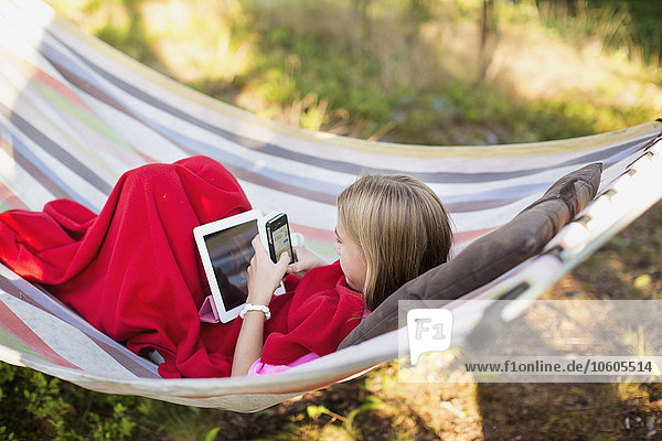 Mädchen mit Mobiltelefon und digitalem Tablet in der Hängematte