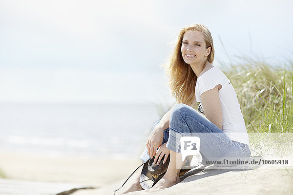 Junge Frau sitzt am Strand mit Meer im Hintergrund