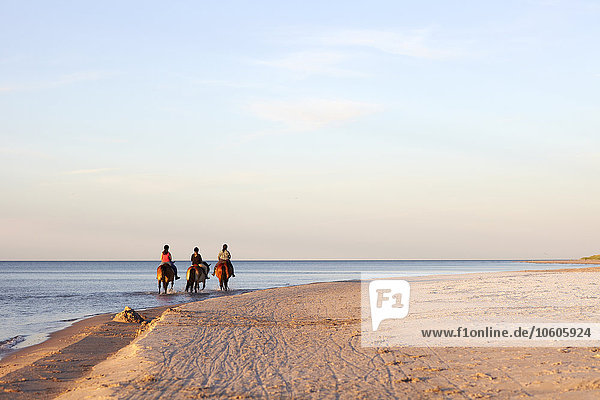 Three women horseback riding on beach
