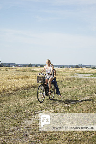 Two girls riding bike through field