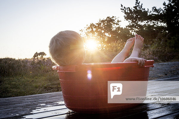 Small boy lying in baby bathtub at sunset