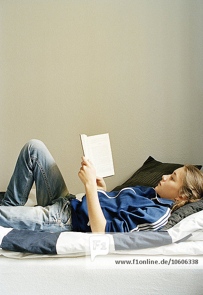 Thirteen-year-old girl lying in her bed reading a book  Stockholm  Sweden.