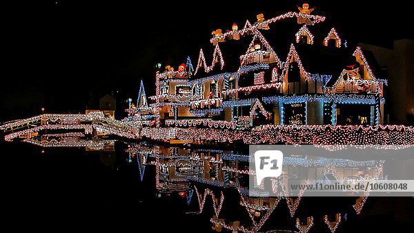 Mit Weihnachtslichtern geschmücktes Haus  das sich nachts im Wasser spiegelt